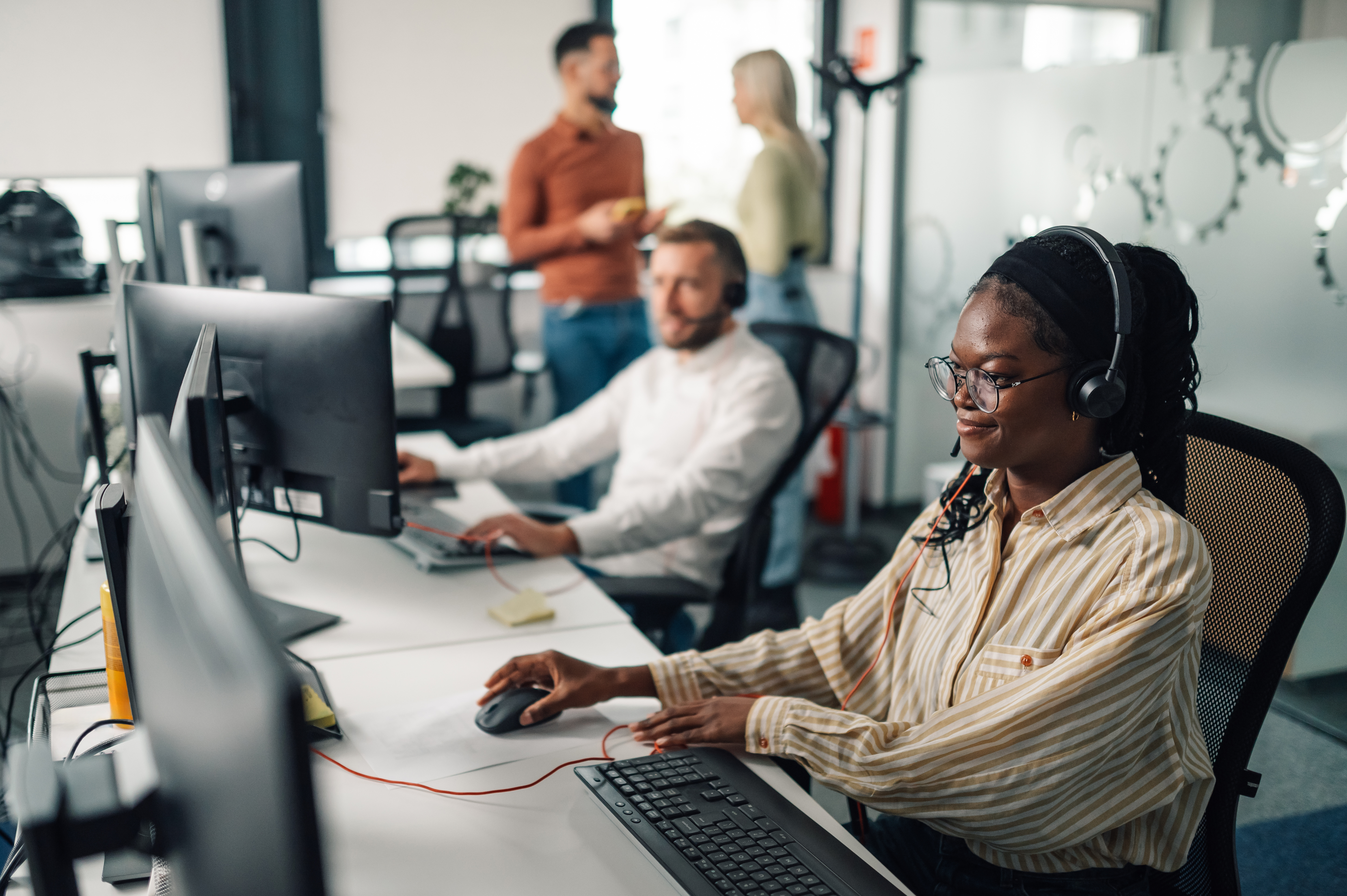 Woman in office support role surrounded by other people working